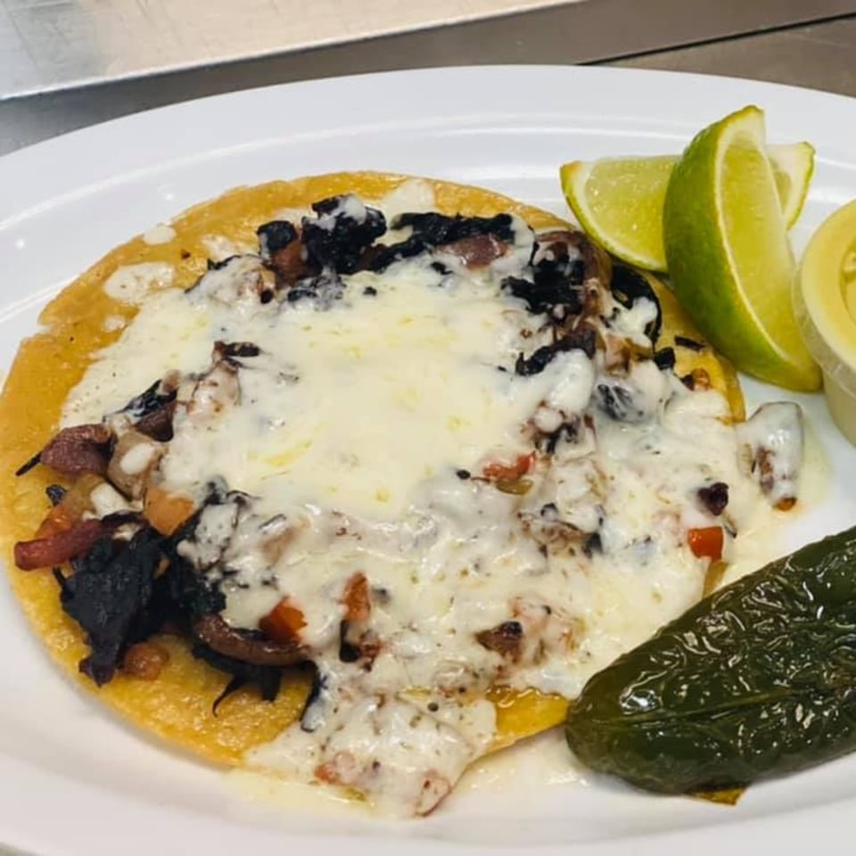 Catrina's Mexican Food taco with melted cheese, dark filling, lime wedges, and a grilled jalapeño.