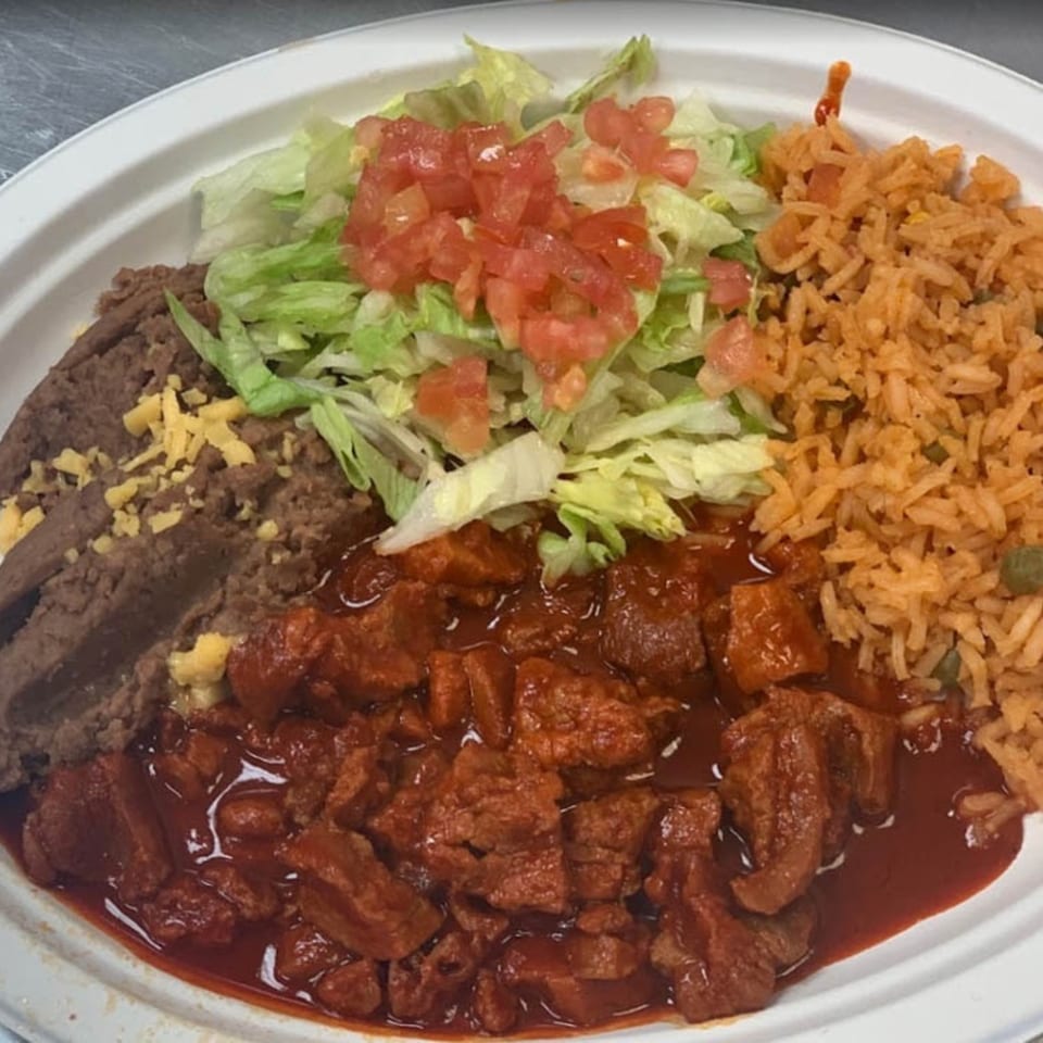 A plate of Catrina's Mexican Food with chile colorado, refried beans, rice, lettuce, and diced tomatoes.