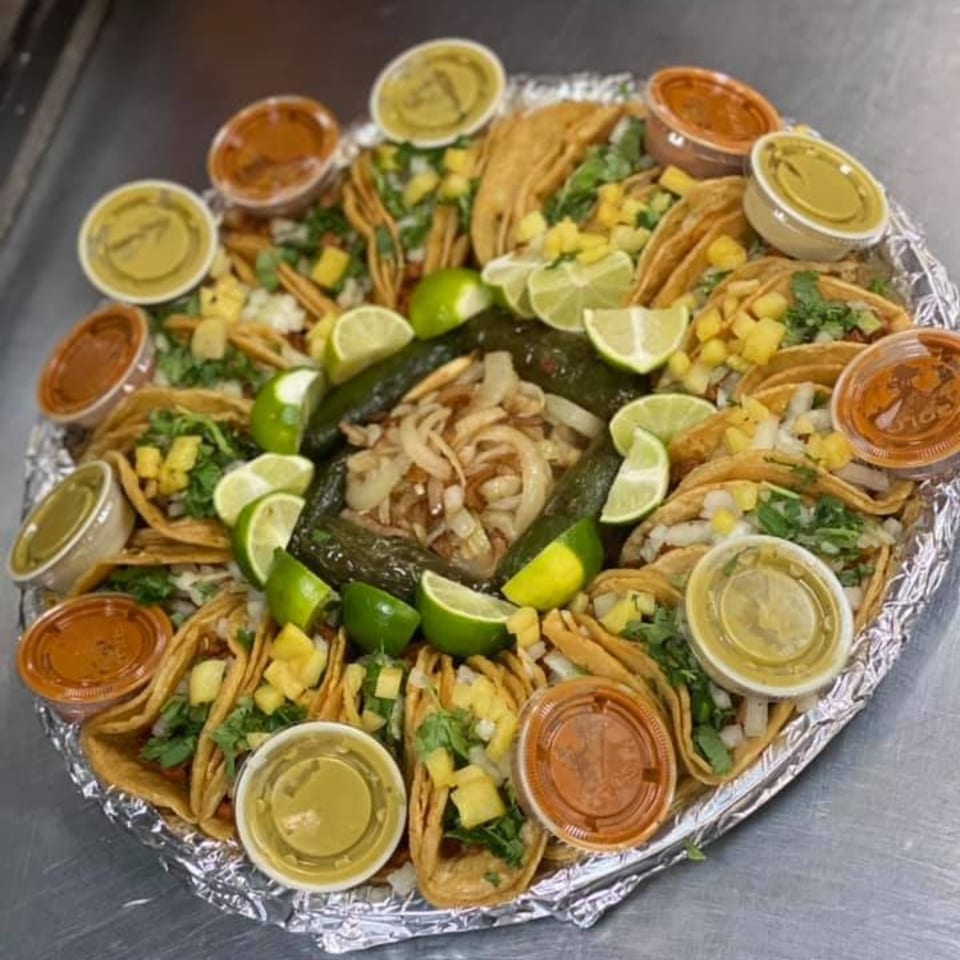 A large platter of Catrina's Mexican Food tacos, salsas, grilled peppers, onions, and lime wedges.