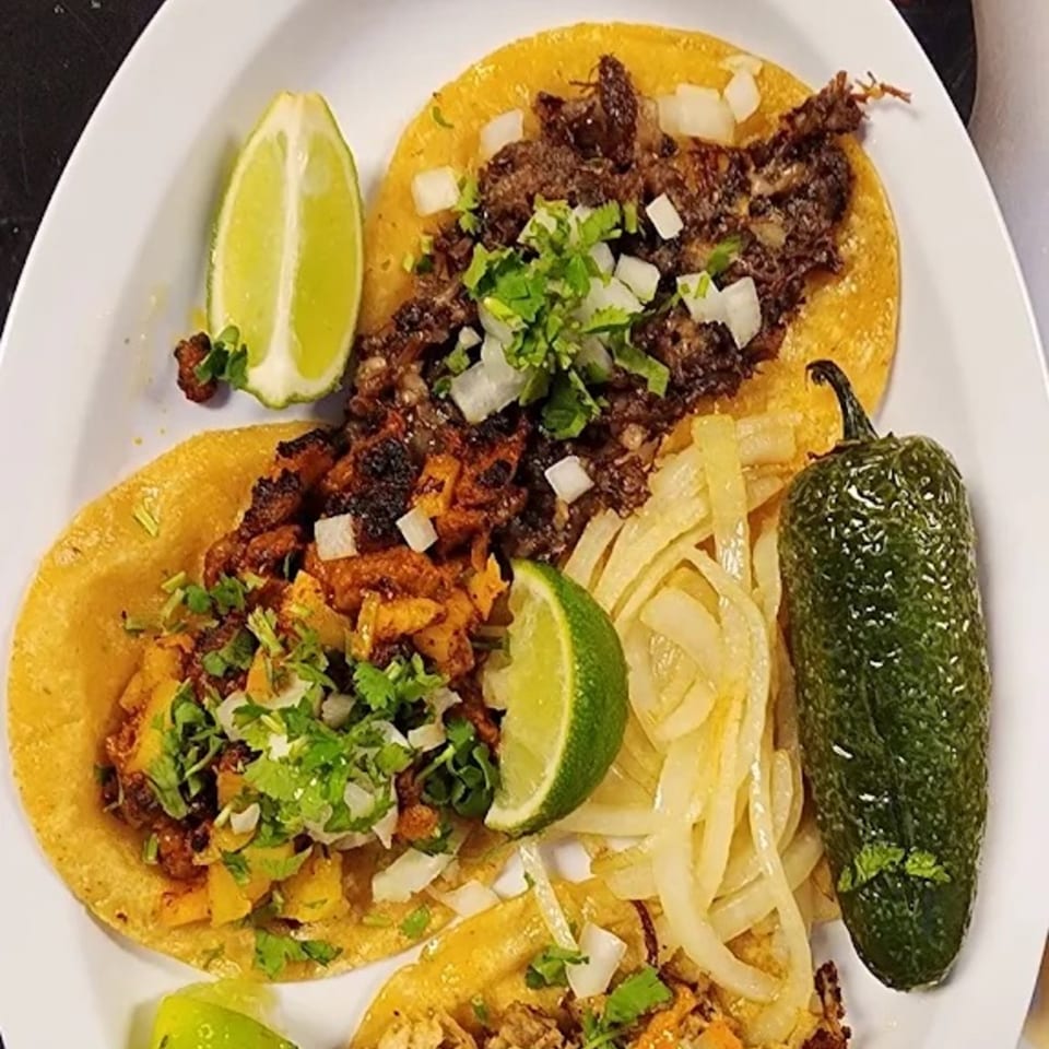 Three Catrina's Mexican Food tacos with meat, cilantro, onions, lime wedges, and a jalapeño.