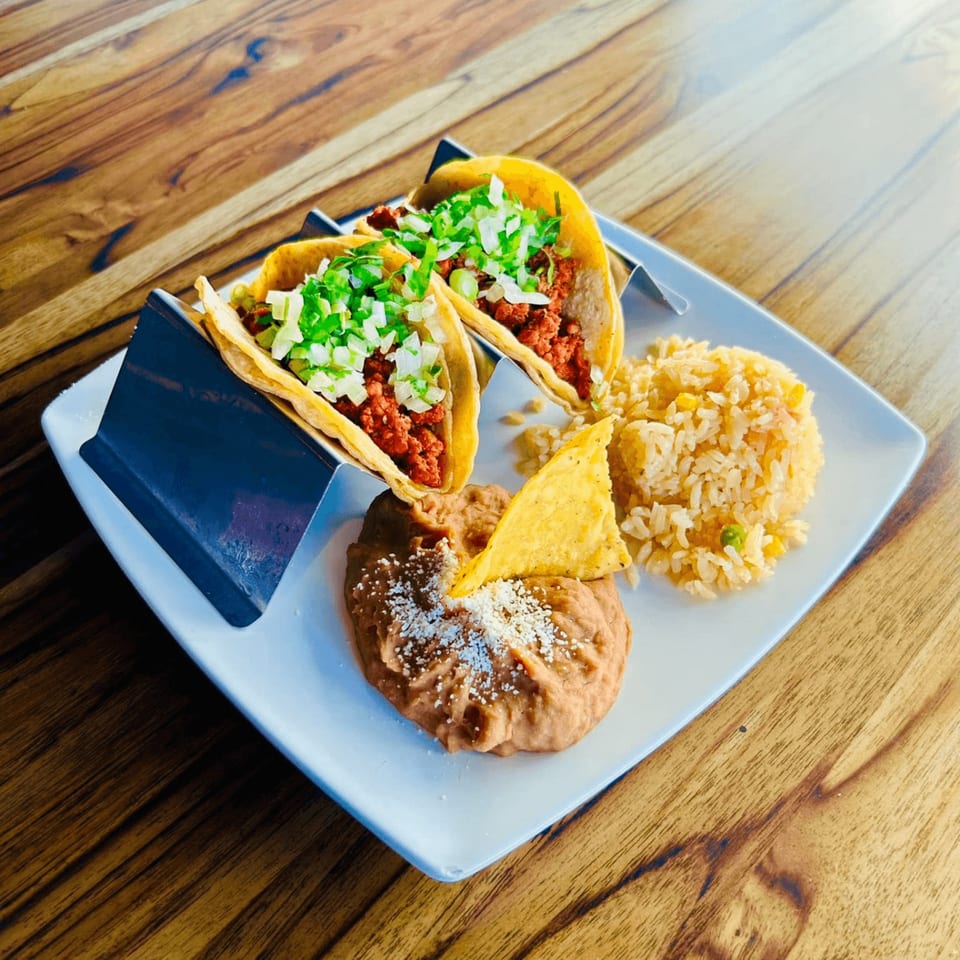 Two Catrina's Mexican Food tacos with rice and refried beans on a white plate.